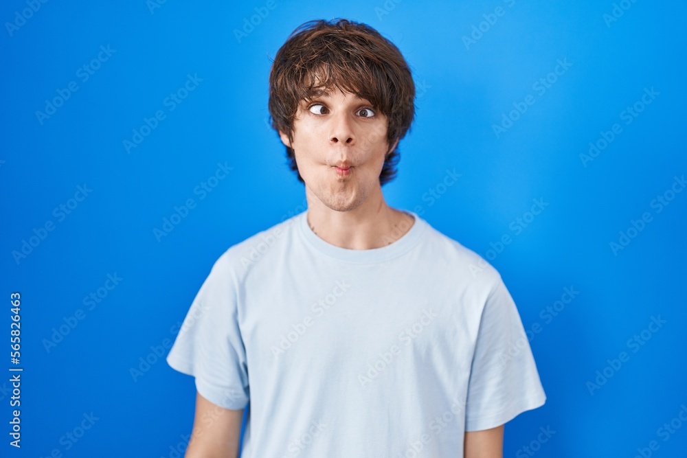 Hispanic young man standing over blue background making fish face with lips, crazy and comical gesture. funny expression. Hispanic young man standing over blue background making fish face with lips, crazy and comical gesture. funny expression.