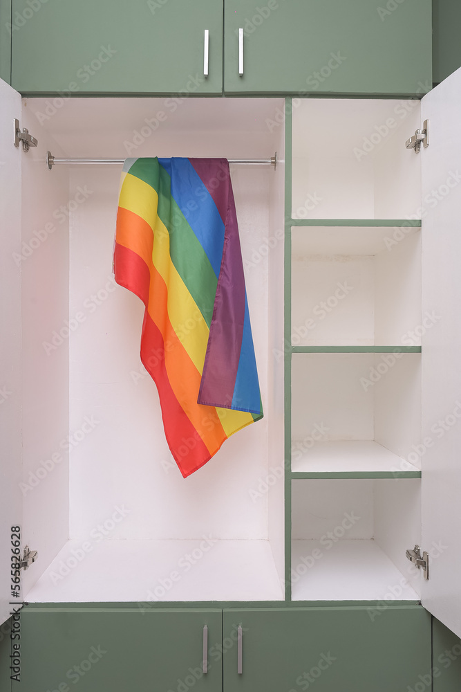 Rainbow flag hangs inside a closet, doors open. Fear of coming out