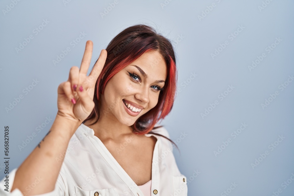 Young caucasian woman wearing casual white shirt over isolated background smiling looking to the camera showing fingers doing victory sign. number two. Young caucasian woman wearing casual white shirt over isolated background smiling looking to the camera showing fingers doing victory sign. number two.