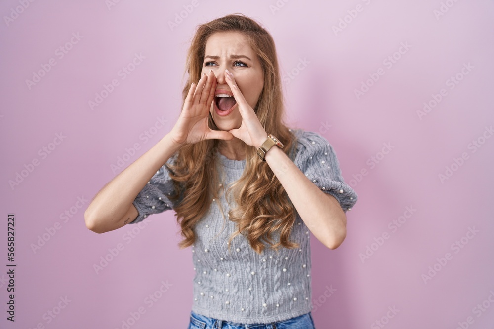 Beautiful blonde woman standing over pink background shouting angry out loud with hands over mouth Beautiful blonde woman standing over pink background shouting angry out loud with hands over mouth