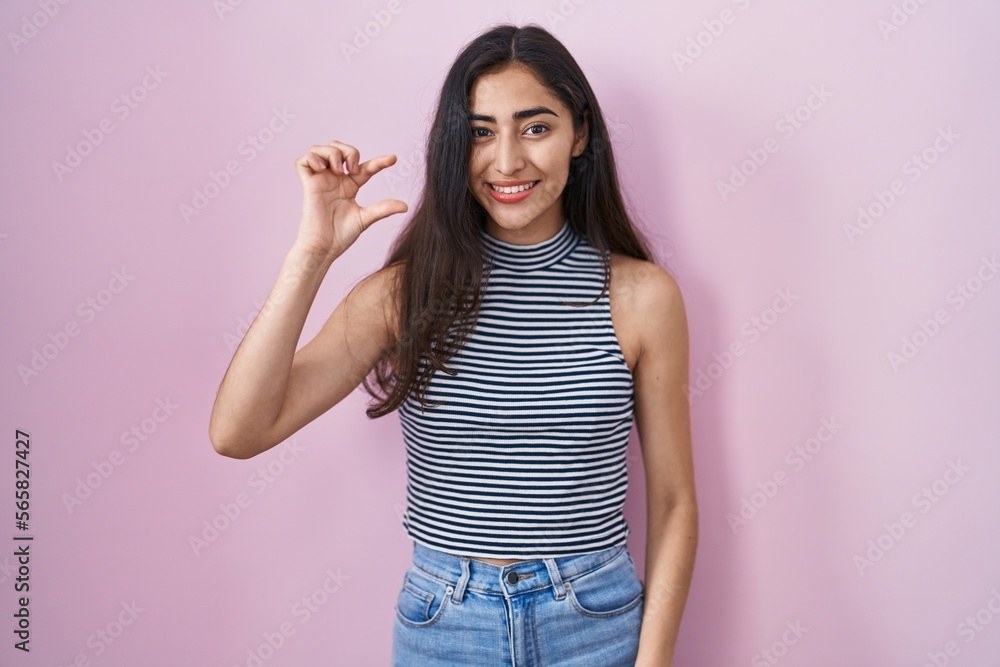 Young teenager girl wearing casual striped t shirt smiling and confident gesturing with hand doing small size sign with fingers looking and the camera. measure concept. Young teenager girl wearing casual striped t shirt smiling and confident gesturing with hand doing small size sign with fingers looking and the camera. measure concept.