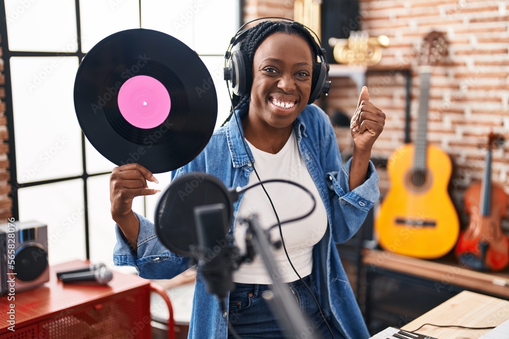 Beautiful black woman holding vinyl record at music studio screaming proud, celebrating victory and success very excited with raised arm Beautiful black woman holding vinyl record at music studio screaming proud, celebrating victory and success very excited with raised arm