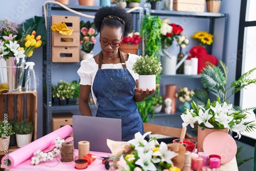 African american woman florist using laptop holding plant at florist store