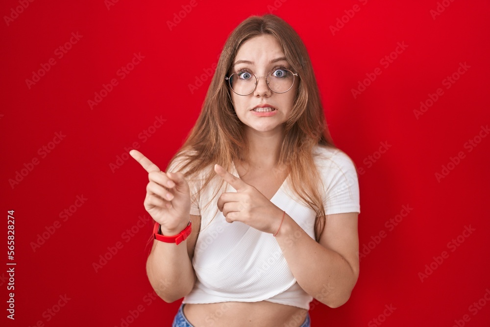Young caucasian woman standing over red background pointing aside worried and nervous with both hands, concerned and surprised expression Young caucasian woman standing over red background pointing aside worried and nervous with both hands, concerned and surprised expression