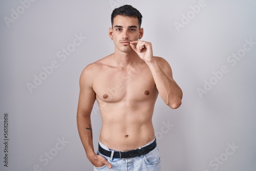 Handsome hispanic man standing shirtless mouth and lips shut as zip with fingers. secret and silent, taboo talking
