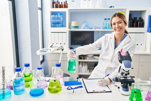 Young hispanic woman scientist measuring liquid write on document at laboratory