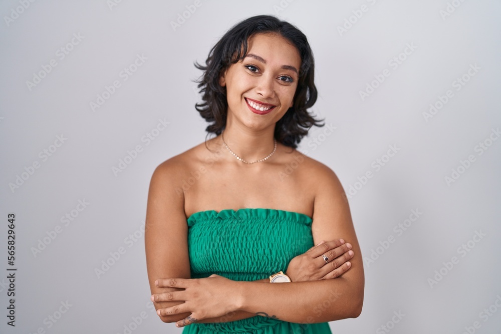 Young hispanic woman standing over isolated background happy face smiling with crossed arms looking at the camera. positive person. Young hispanic woman standing over isolated background happy face smiling with crossed arms looking at the camera. positive person.