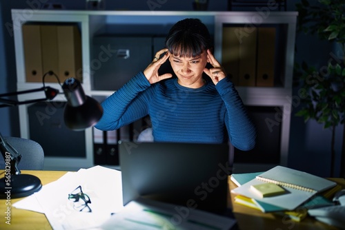 Young beautiful woman working at the office at night covering ears with fingers with annoyed expression for the noise of loud music. deaf concept.