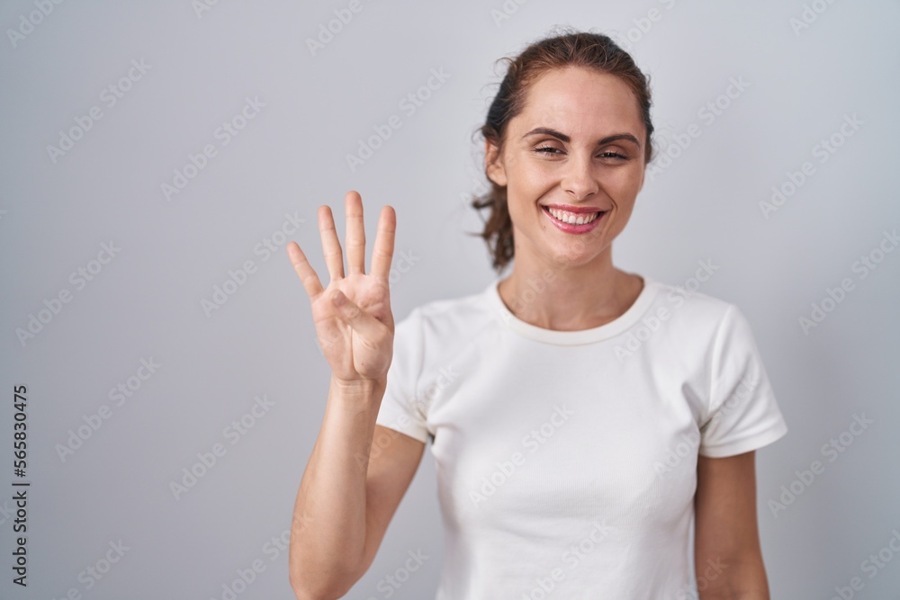 Beautiful brunette woman standing over isolated background showing and pointing up with fingers number four while smiling confident and happy.