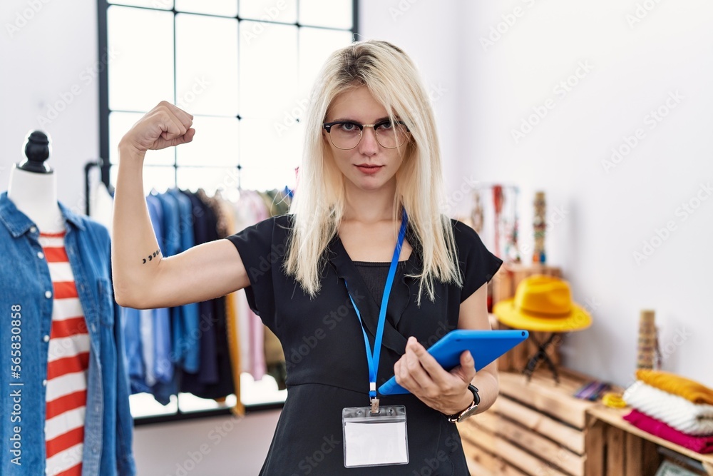Young blonde woman working as manager at retail boutique strong person showing arm muscle, confident and proud of power Young blonde woman working as manager at retail boutique strong person showing arm muscle, confident and proud of power