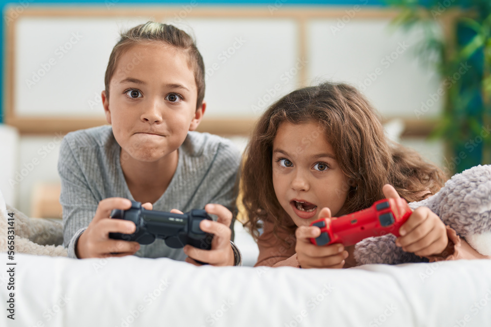 Two kids playing video game lying on bed at bedroom Two kids playing video game lying on bed at bedroom