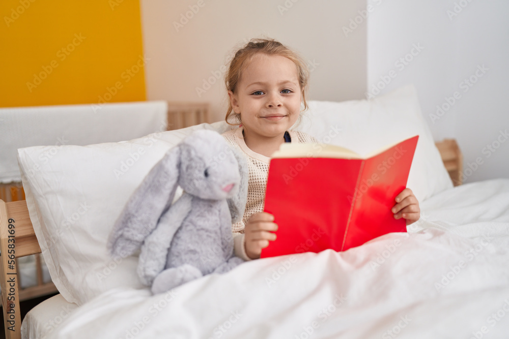 Adorable blonde girl reading book sitting on bed at bedroom Adorable blonde girl reading book sitting on bed at bedroom
