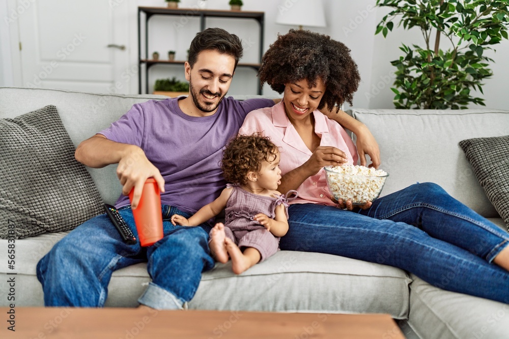 Couple and daughter watching movie sitting on sofa at home Couple and daughter watching movie sitting on sofa at home