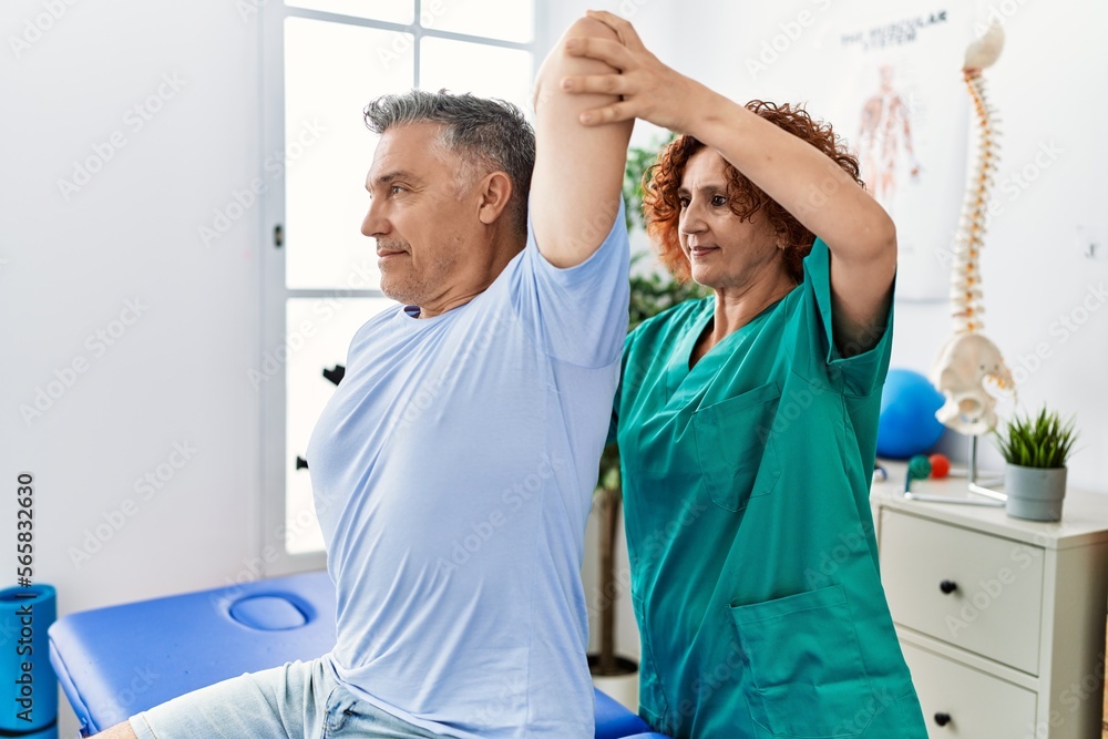Obraz premium Middle age man and woman wearing physiotherapy uniform having rehab session stretching arm at physiotherapy clinic