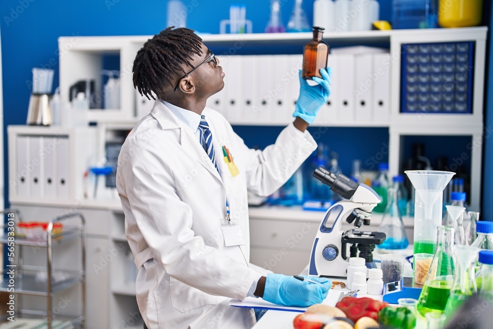 African american man scientist writing report holding bottle at laboratory African american man scientist writing report holding bottle at laboratory