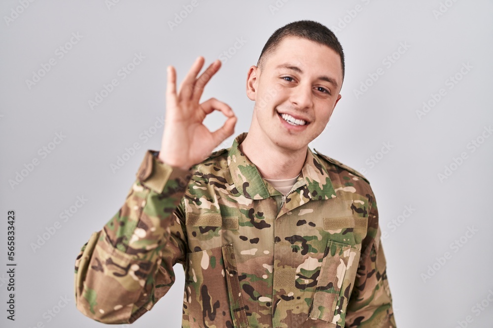 Young man wearing camouflage army uniform smiling positive doing ok sign with hand and fingers. successful expression. Young man wearing camouflage army uniform smiling positive doing ok sign with hand and fingers. successful expression.