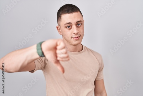 Young man standing over isolated background looking unhappy and angry showing rejection and negative with thumbs down gesture. bad expression.