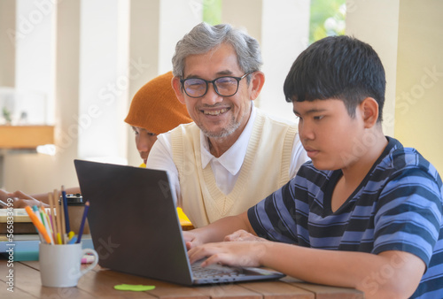 mature father helping his teen sons to do school project on computer laptop, happy asian family working together at home