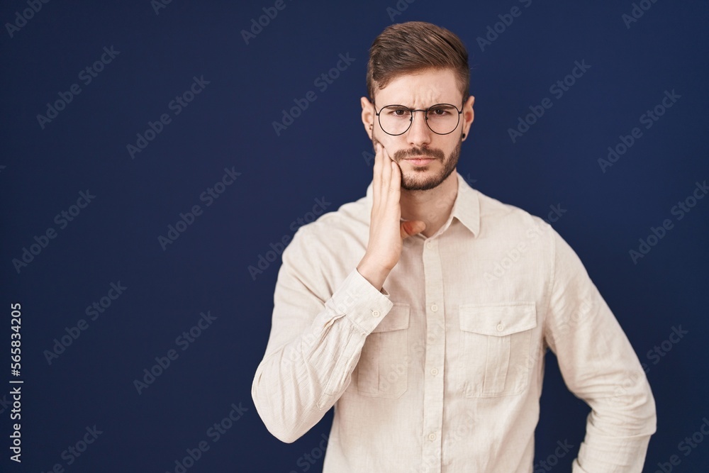 Hispanic man with beard standing over blue background touching mouth with hand with painful expression because of toothache or dental illness on teeth. dentist