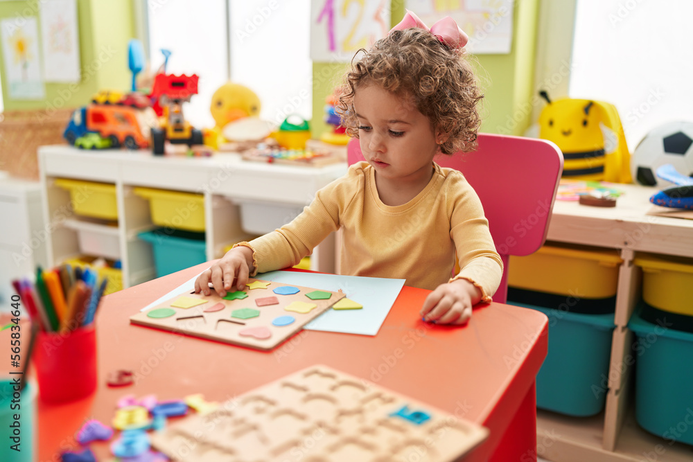 Fototapeta premium Adorable hispanic toddler playing with maths puzzle game sitting on table at kindergarten