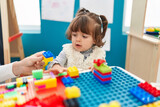 Adorable hispanic toddler playing with construction blocks sitting on table at kindergarten