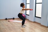 Young african american woman smiling confident training using dumbbells at sport center