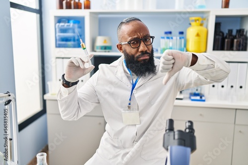 African american man working at scientist laboratory holding syringe with angry face, negative sign showing dislike with thumbs down, rejection concept