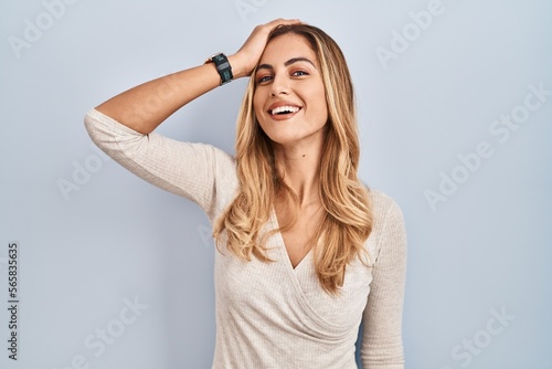 Young blonde woman standing over isolated background smiling confident touching hair with hand up gesture, posing attractive and fashionable