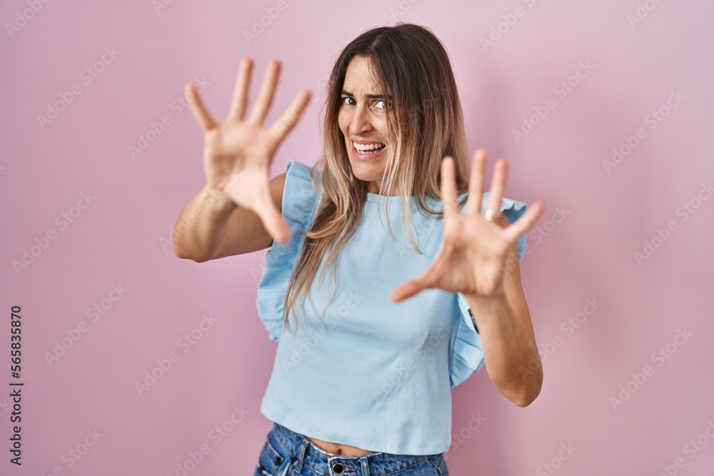 Young hispanic woman standing over pink background afraid and terrified with fear expression stop gesture with hands, shouting in shock. panic concept. Young hispanic woman standing over pink background afraid and terrified with fear expression stop gesture with hands, shouting in shock. panic concept.