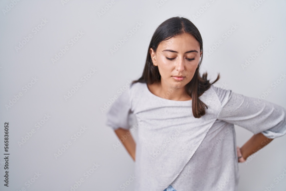 Young hispanic woman standing over white background suffering of backache, touching back with hand, muscular pain Young hispanic woman standing over white background suffering of backache, touching back with hand, muscular pain
