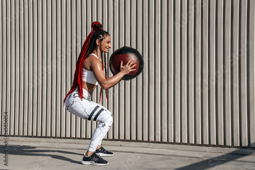 Athletic woman doing exercise squat with med ball. Strength and motivation.Photo of sporty woman in fashionable sportswear