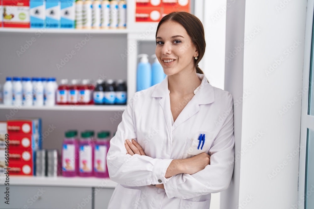 Young woman pharmacist standing with arms crossed gesture at pharmacy