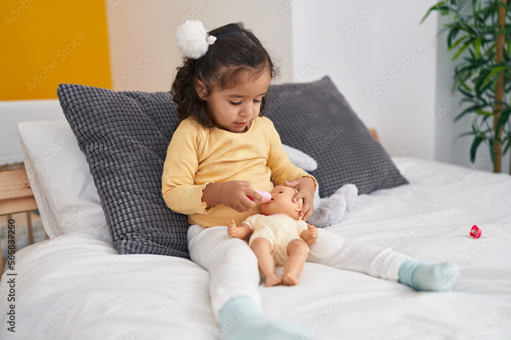Adorable hispanic toddler playing with baby doll sitting on bed at bedroom Adorable hispanic toddler playing with baby doll sitting on bed at bedroom