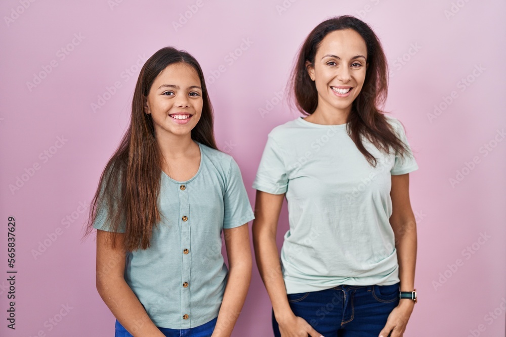 Young mother and daughter standing over pink background with a happy and cool smile on face. lucky person. Young mother and daughter standing over pink background with a happy and cool smile on face. lucky person.