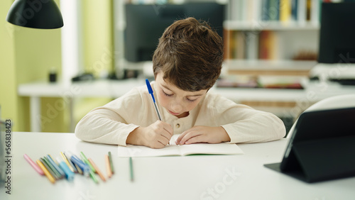 Adorable hispanic boy student sitting on table doing homework at classroom