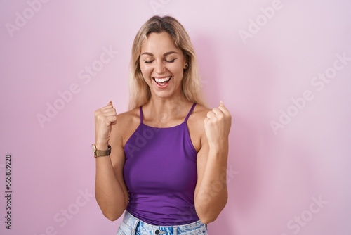 Young blonde woman standing over pink background very happy and excited doing winner gesture with arms raised  smiling and screaming for success. celebration concept.