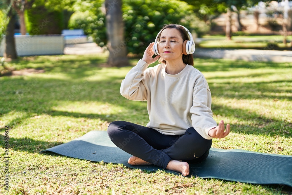 Middle age woman doing yoga exercise sitting on herb at park Middle age woman doing yoga exercise sitting on herb at park