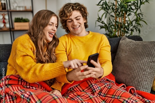 Young caucasian couple using smartphone sitting on sofa at home