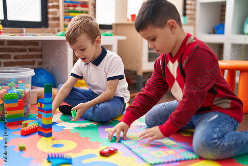 Two kids playing with construction blocks and maths puzzle game sitting on floor at kindergarten