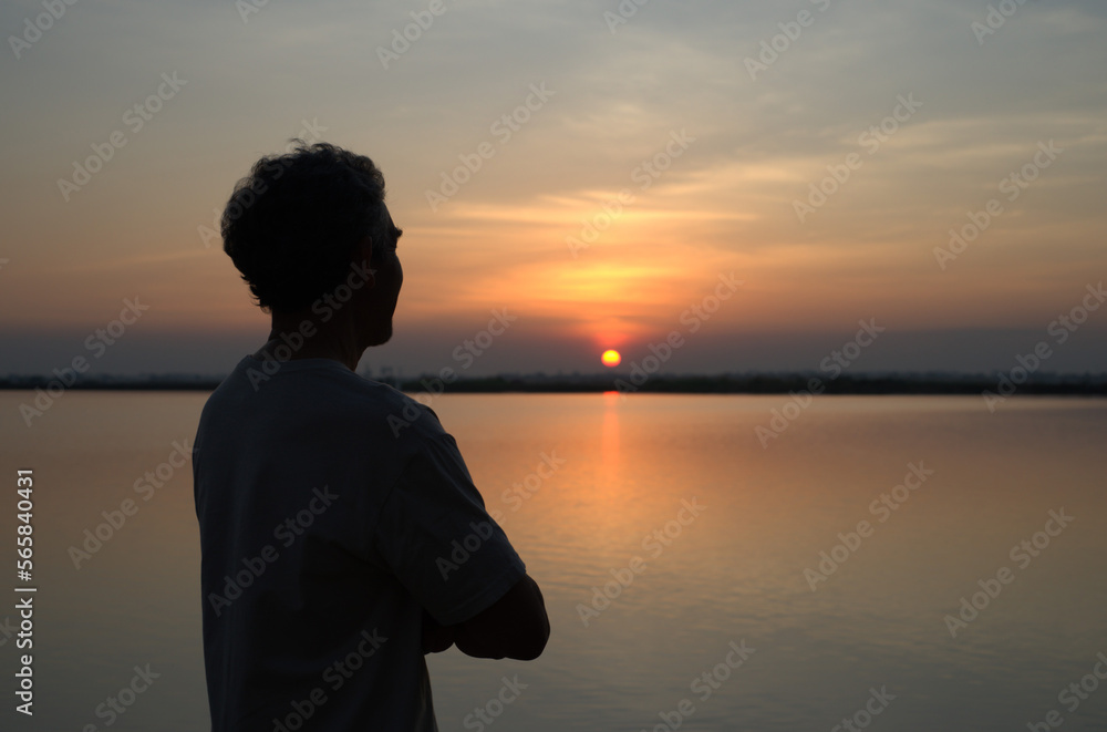healthy mature man after exercise, resting,relaxing,standing by the pond and looking at sunset