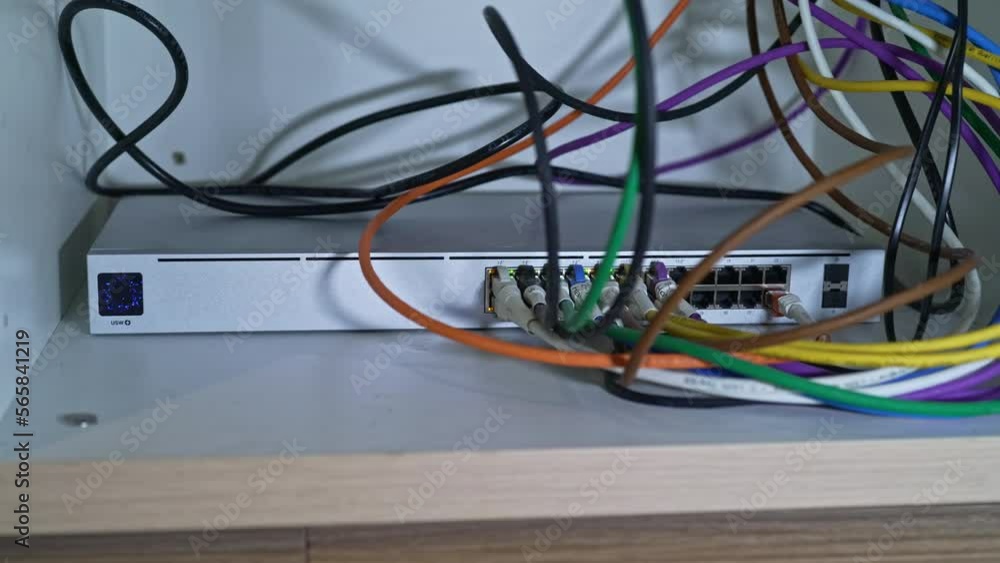 Gray metal power over ethernet Switch with colorful cables at bottom of cupboard indoors of apartment. Movie shot January 29th, 2023, Zurich, Switzerland. Gray metal power over ethernet Switch with colorful cables at bottom of cupboard indoors of apartment. Movie shot January 29th, 2023, Zurich, Switzerland.