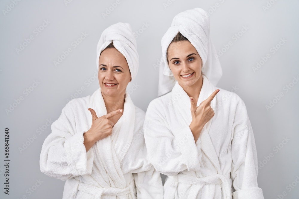 Middle age woman and daughter wearing white bathrobe and towel cheerful with a smile of face pointing with hand and finger up to the side with happy and natural expression on face - obrazy, fototapety, plakaty 