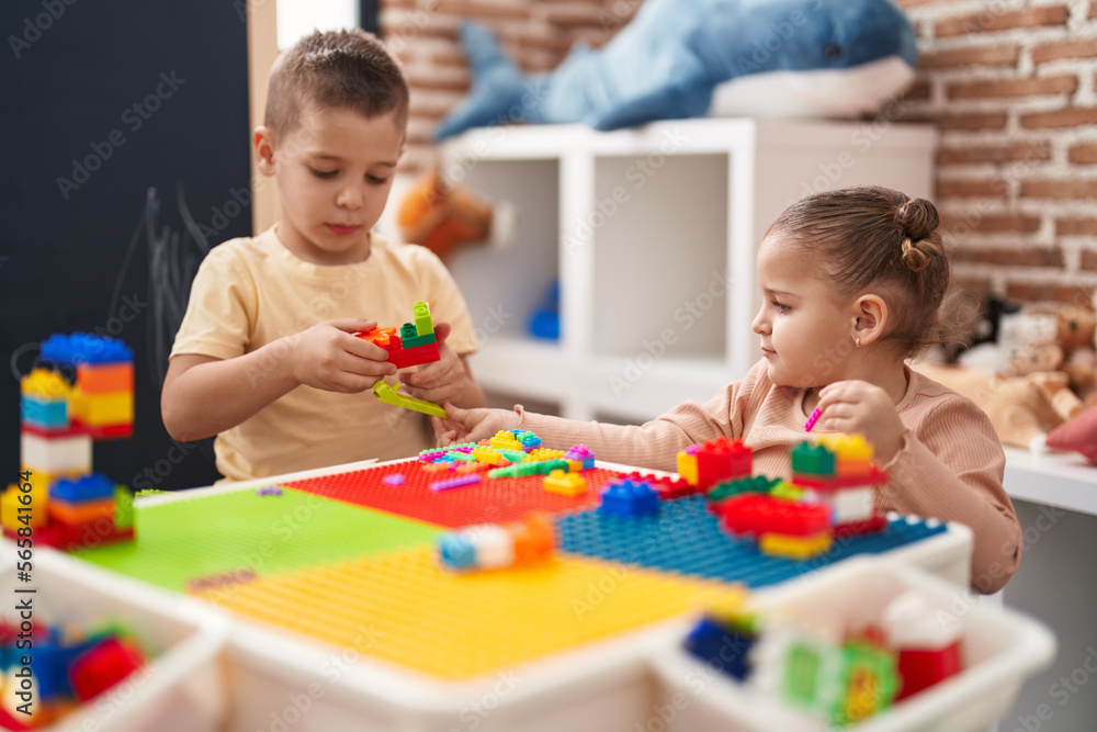 Fototapeta premium Two kids playing with construction blocks sitting on table at kindergarten