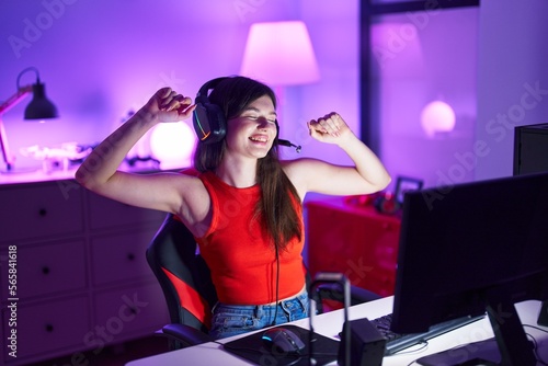 Young caucasian woman streamer playing video game listening music at gaming room