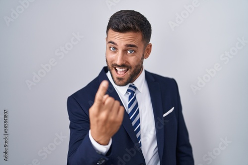 Handsome hispanic man wearing suit and tie beckoning come here gesture with hand inviting welcoming happy and smiling