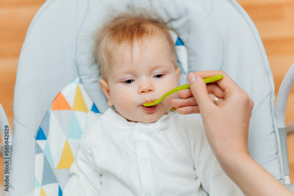 Mother gives fruit sauce to baby.mom feeds baby on highchair.baby food Mother gives fruit sauce to baby.mom feeds baby on highchair.baby food