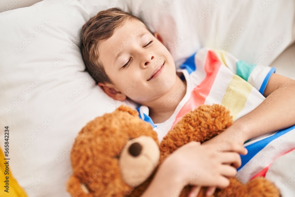 Blond child hugging teddy bear sleeping on bed at bedroom