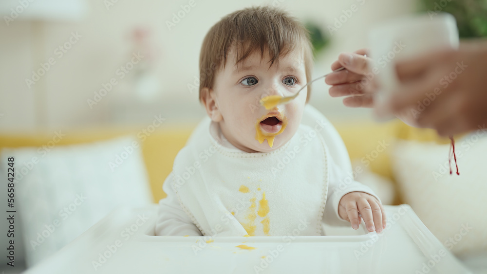 Adorable hispanic toddler sitting on highchair eating food at home Adorable hispanic toddler sitting on highchair eating food at home
