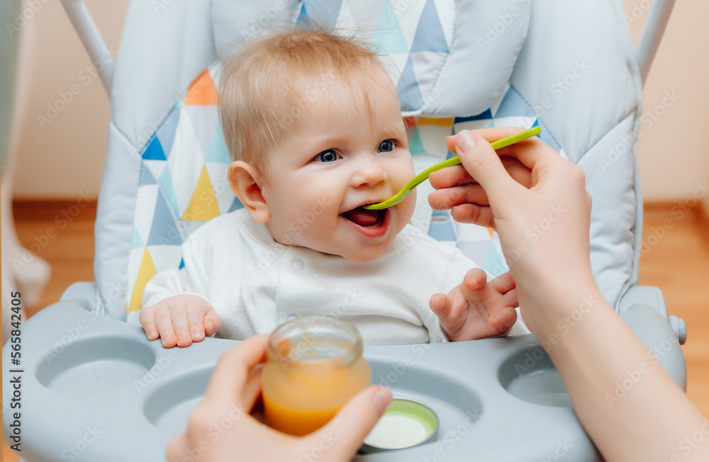 Mother gives fruit sauce to baby.mom feeds baby on highchair.baby food Mother gives fruit sauce to baby.mom feeds baby on highchair.baby food