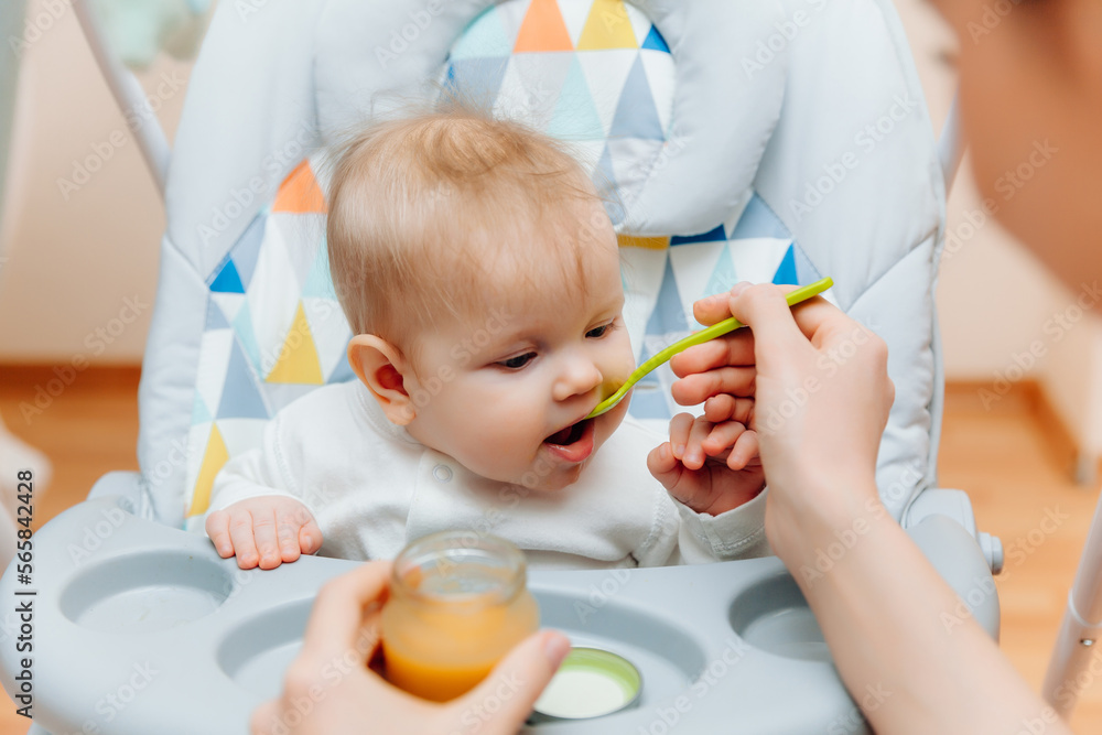 Mother gives fruit sauce to baby.mom feeds baby on highchair.baby food Mother gives fruit sauce to baby.mom feeds baby on highchair.baby food